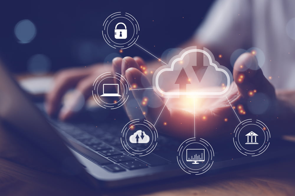 A person working on a laptop with a glowing cloud icon and interconnected symbols representing data transfer, security, and technology floating above their hand - Managed IT Cloud Services